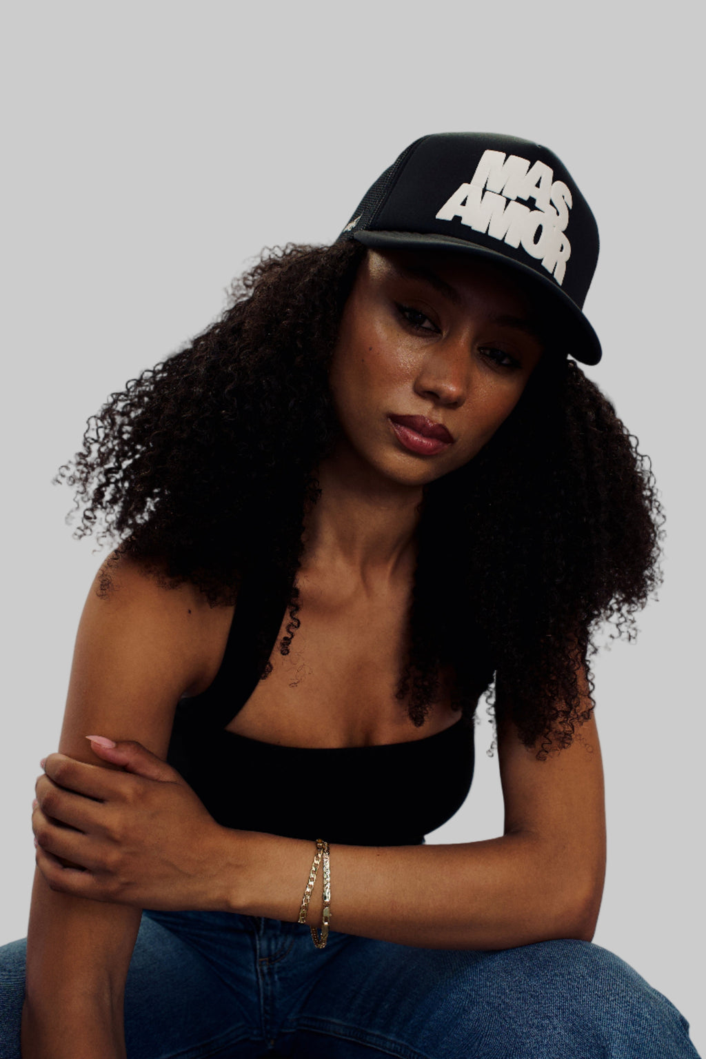 Woman wearing a black cap with white text, sitting against a plain background