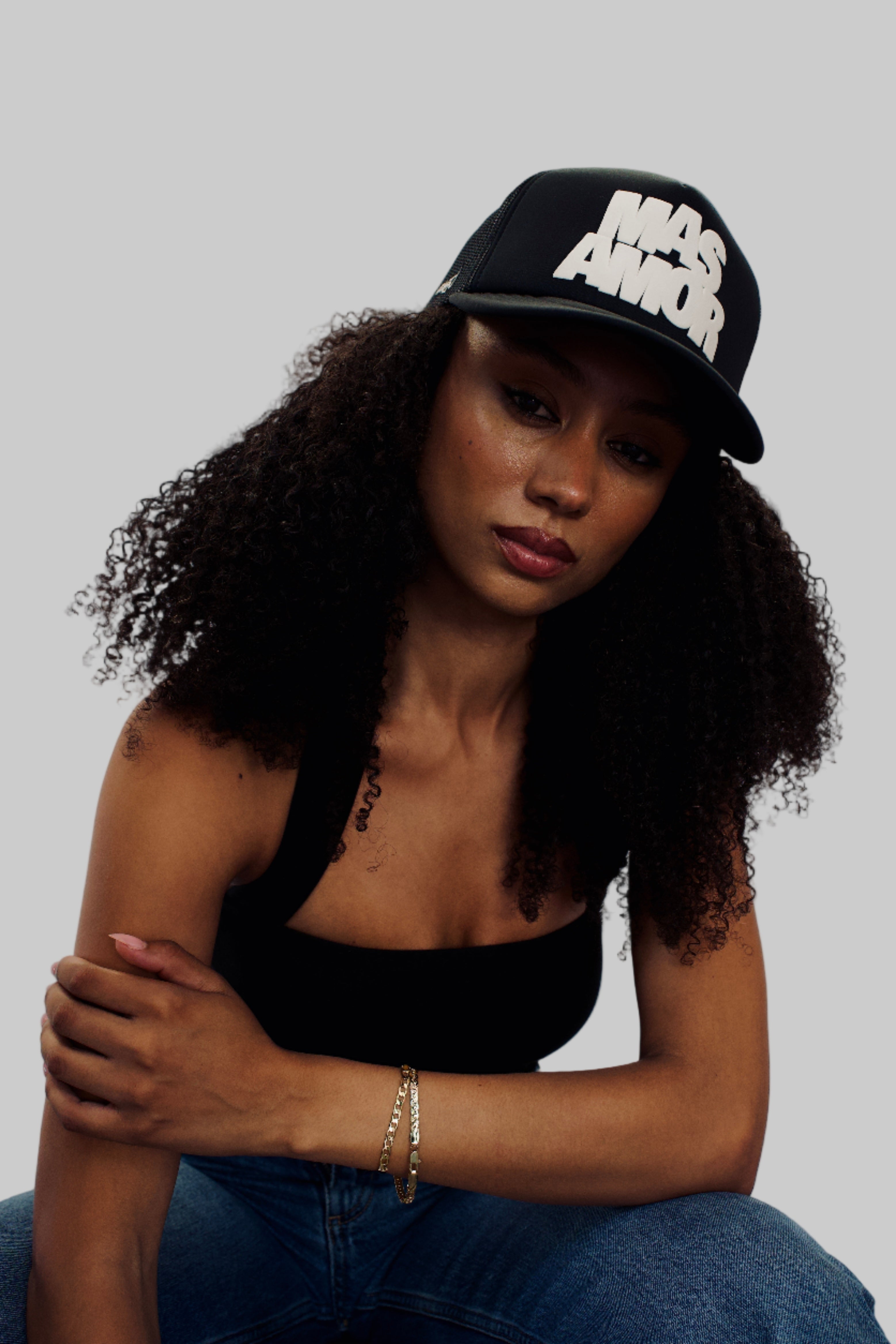 Woman wearing a black cap with white text, sitting against a plain background