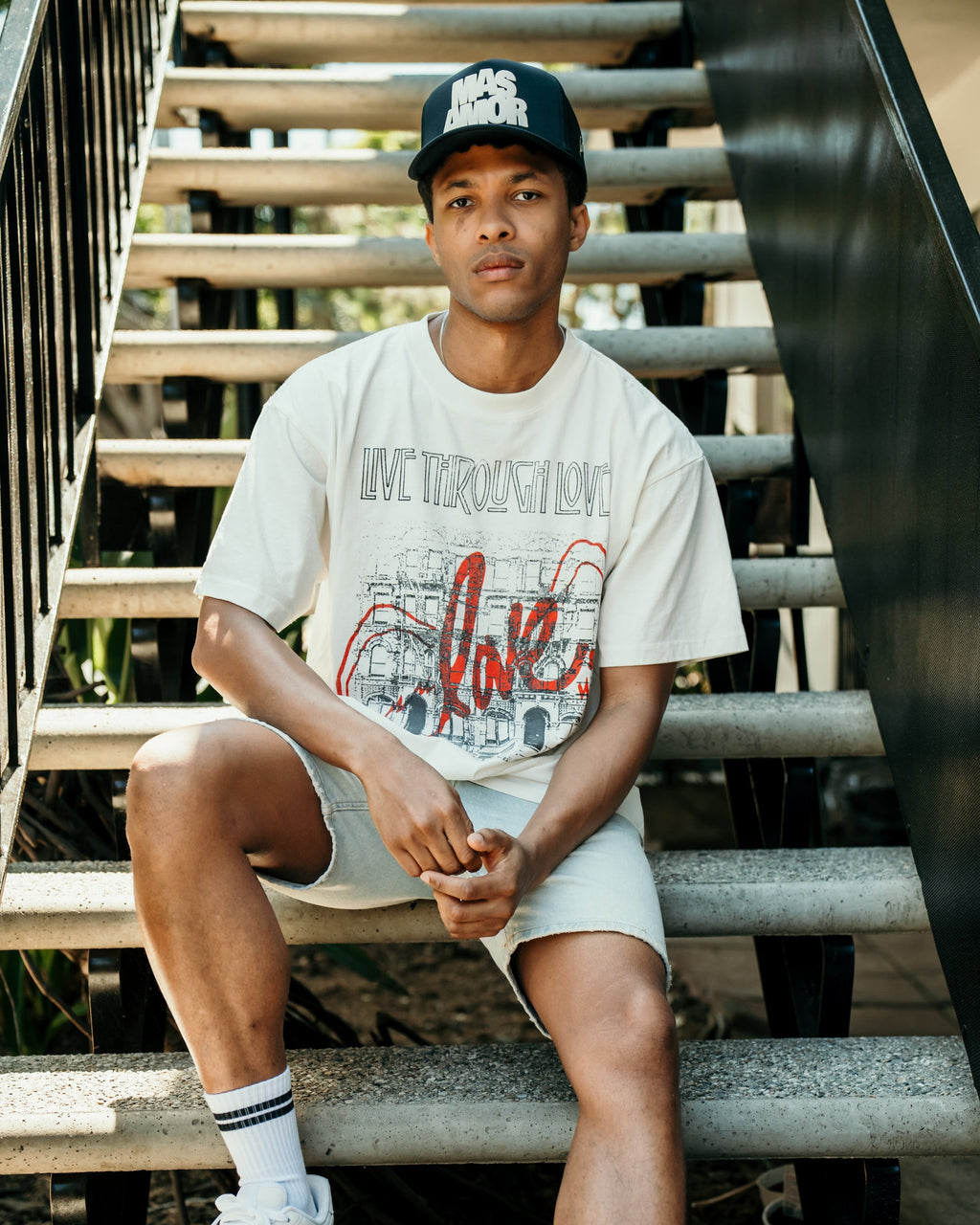 Person wearing a white t-shirt with red text, shorts, and white sneakers sitting on stairs.