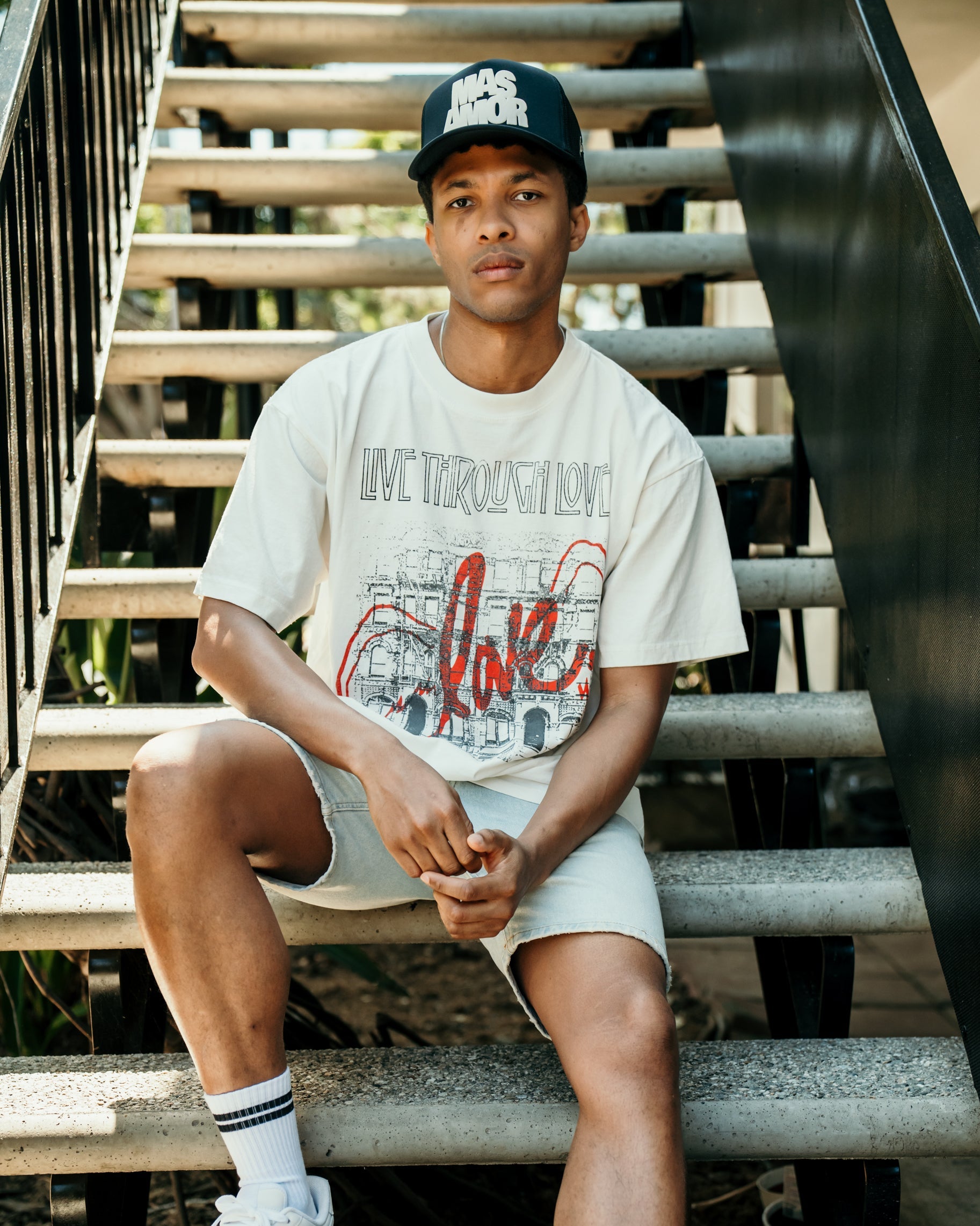 Person wearing a white t-shirt with red text, shorts, and white sneakers sitting on stairs.