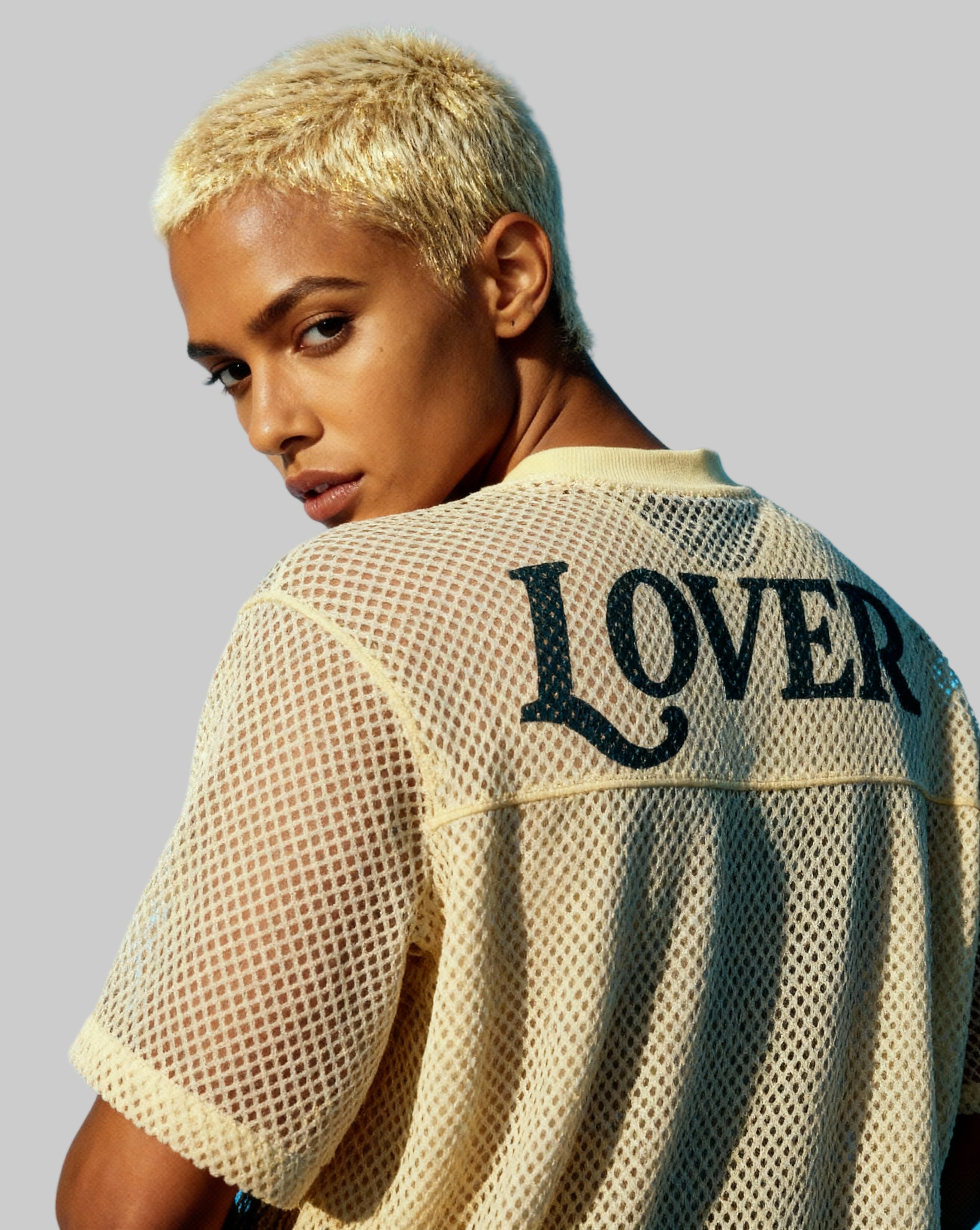 Person wearing a beige mesh shirt with 'LOVER' printed on the back against a blue sky.