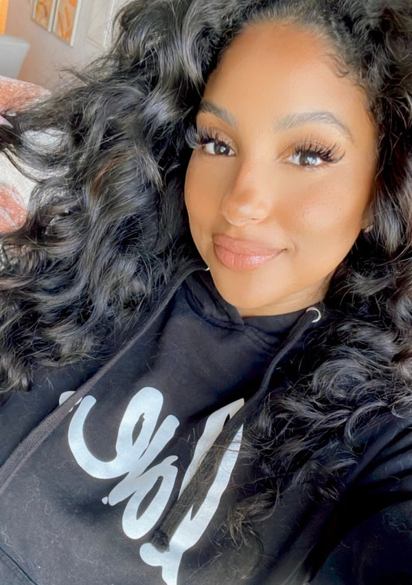 Woman wearing a black hoodie with white text, sitting indoors.