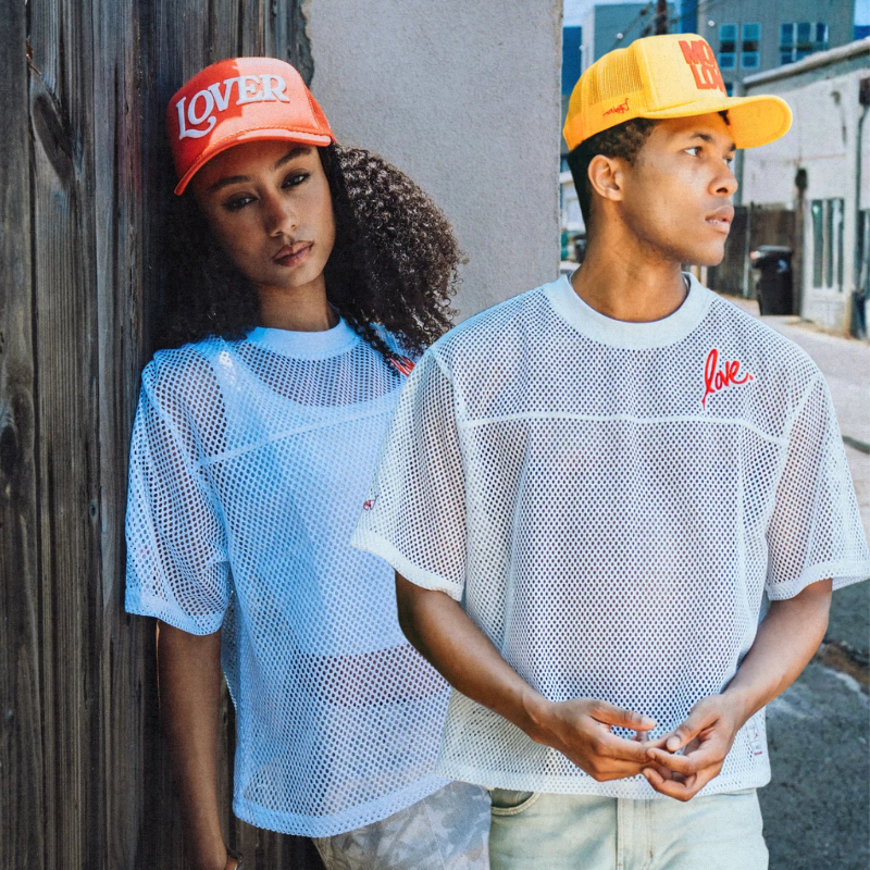 Two people wearing mesh shirts and colorful caps in an urban setting
