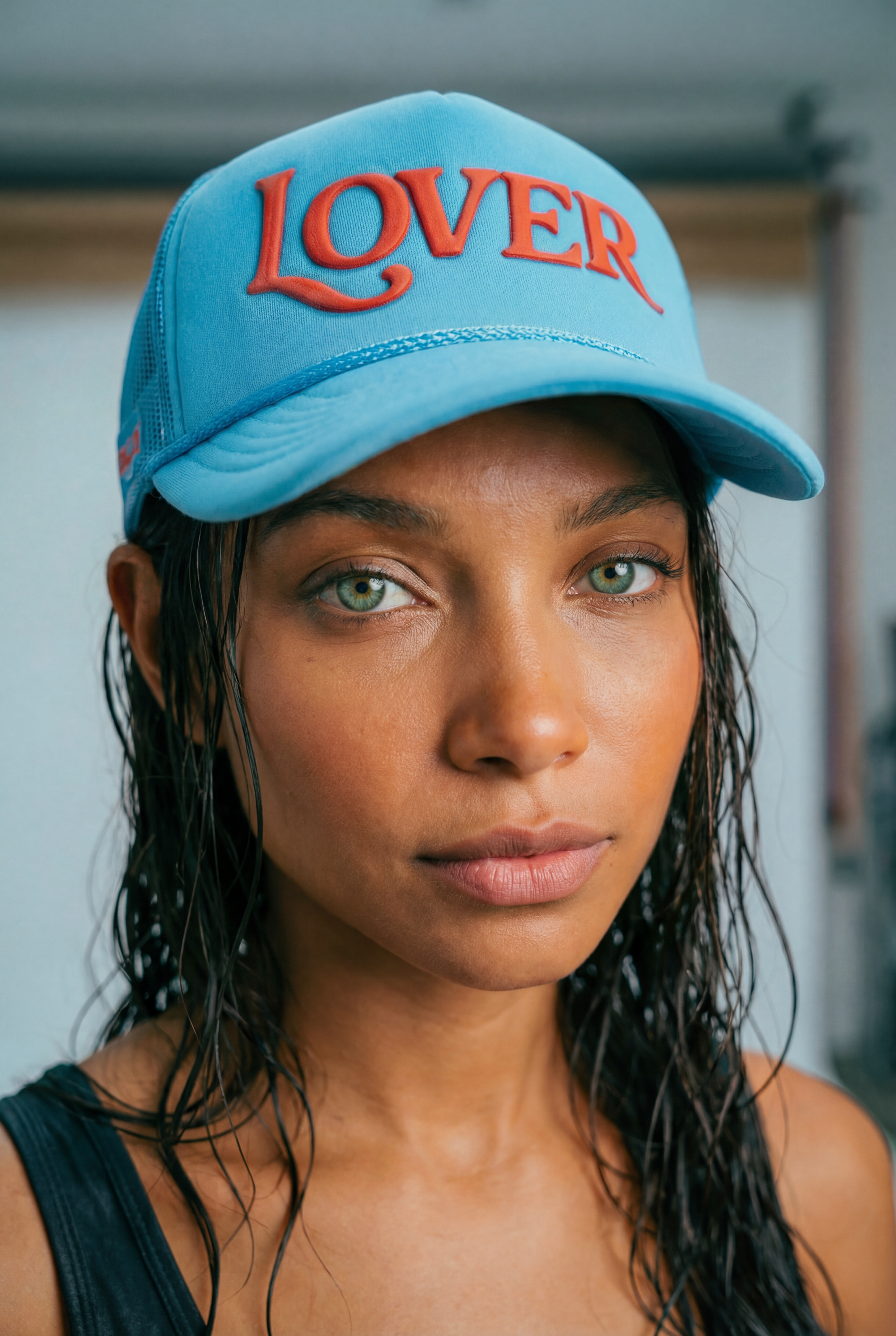 Woman wearing a blue cap with 'LOVER' on it, looking directly at the camera.