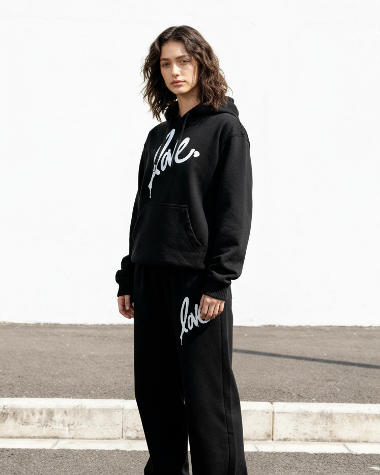 Person wearing a black hoodie and pants with 'love' printed on them, standing on a road.
