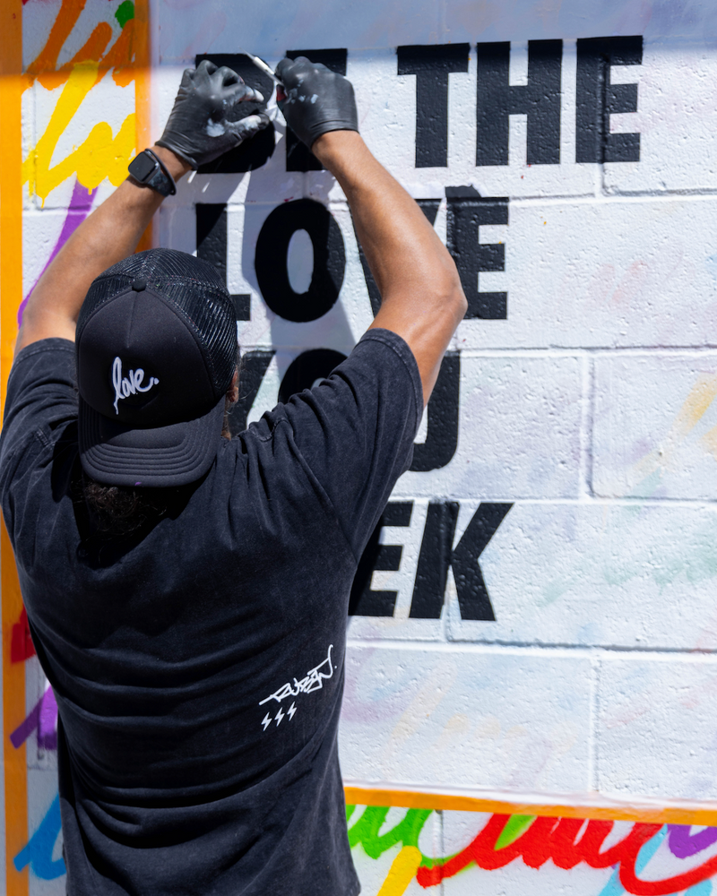 Ruben Rojas painting graffiti on a wall with colorful text and shapes.