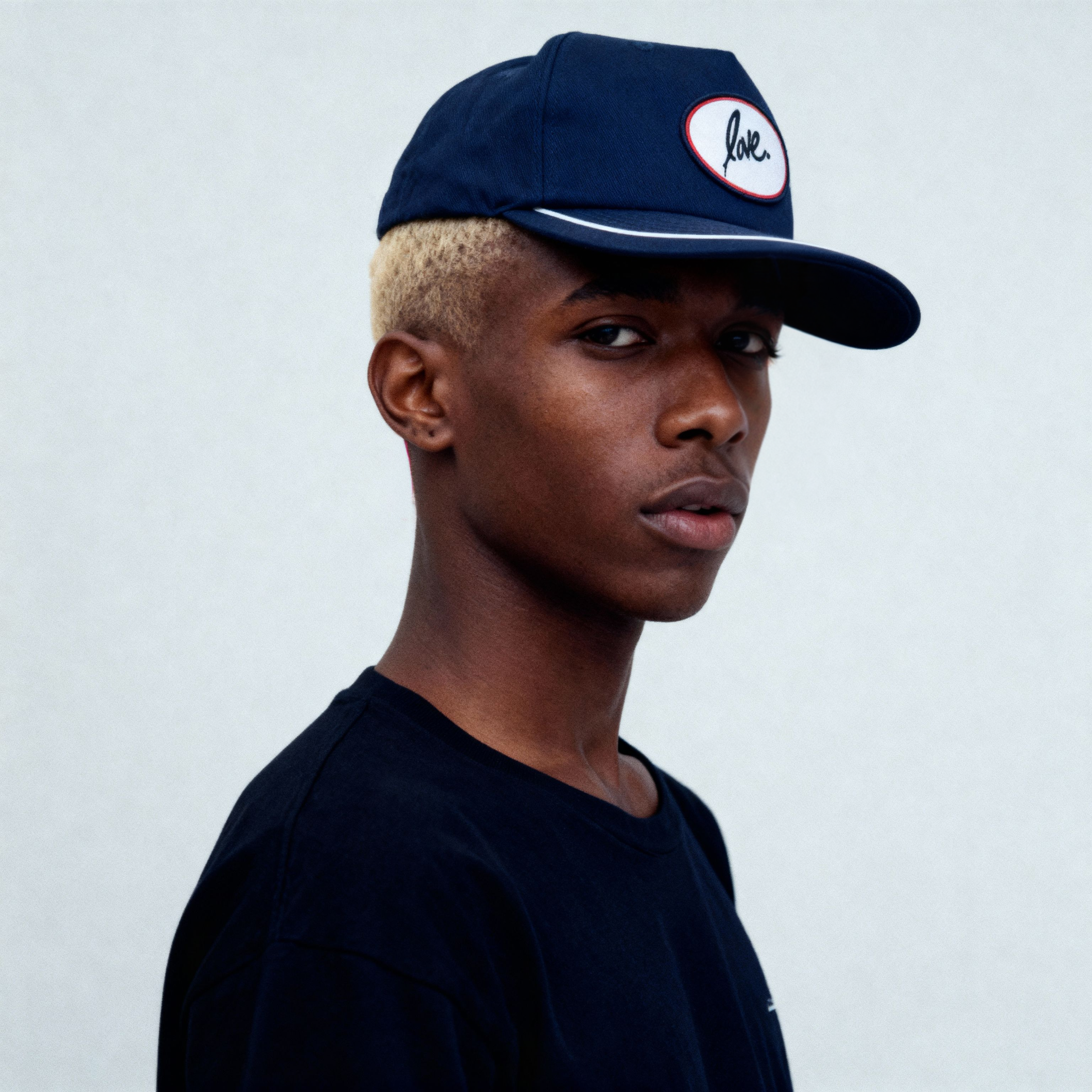 Person wearing a navy cap with a Ruben Rojas love logo on a plain background